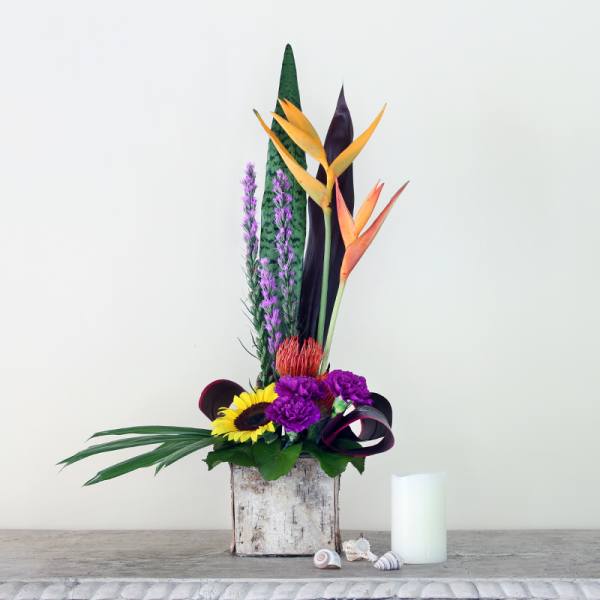 Tropical flower arrangement in a rustic wooden container with a white candle