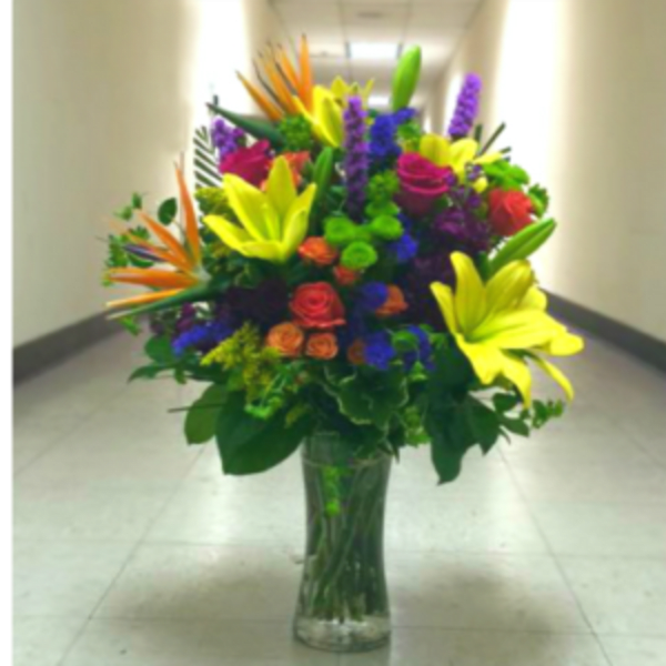 Tall mixed bouquet in a clear glass vase with bright lilies and roses