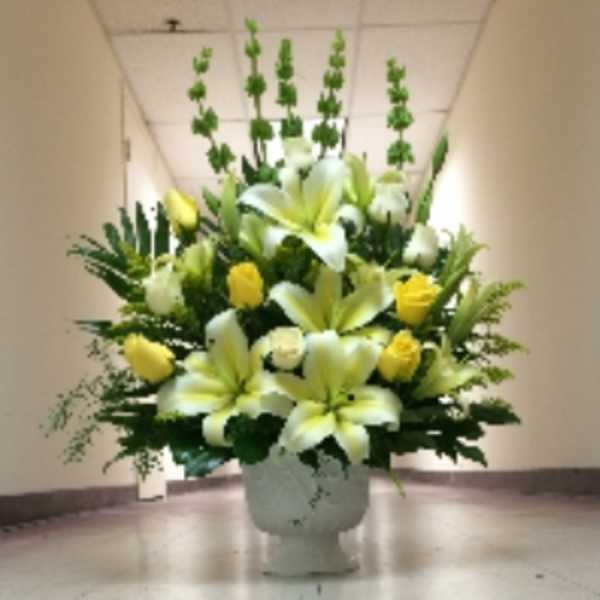 Tall yellow and white lily and rose arrangement in a white urn-style vase