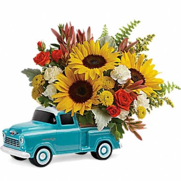 Bright sunflowers and mixed blooms arranged in a turquoise ceramic pickup truck container