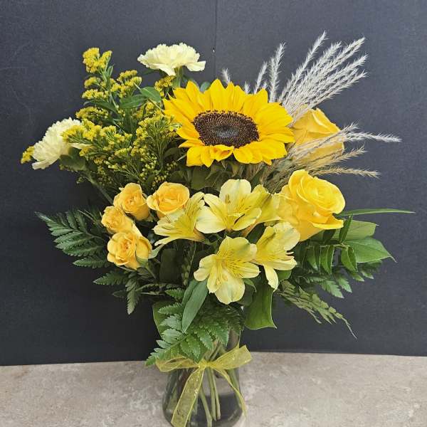 Yellow floral arrangement with a sunflower and roses in a glass vase