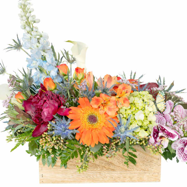 Mixed floral arrangement in a wooden box with orange, blue, and pink blooms