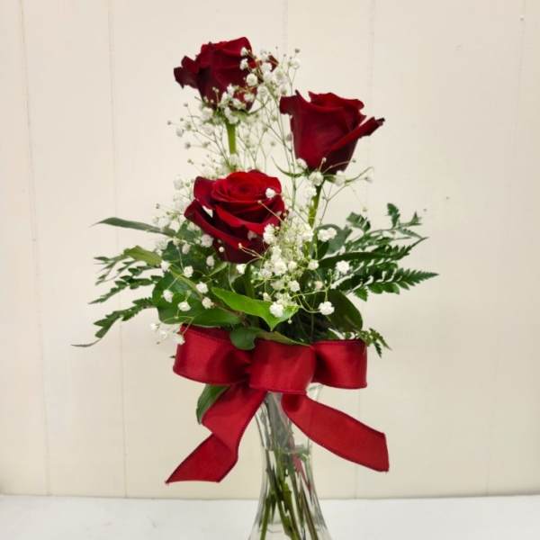 Three red roses in a clear glass vase with a red ribbon