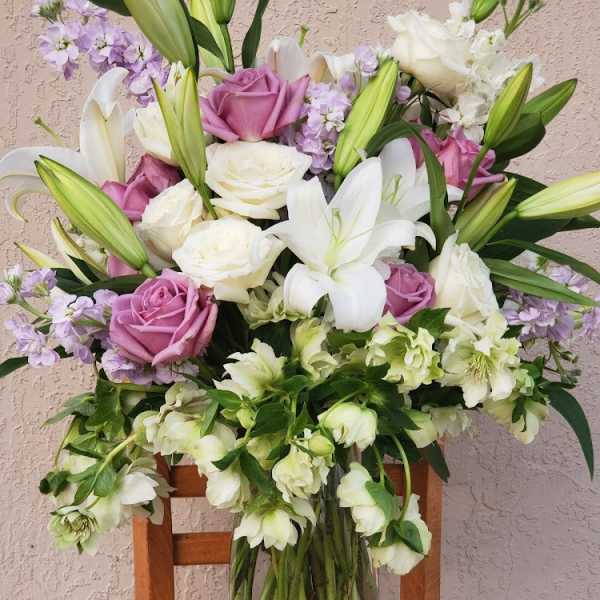 Bouquet of white lilies, pink roses, and lavender flowers in a glass vase