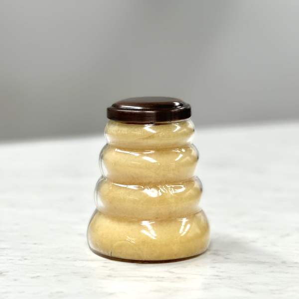 Beehive-shaped plastic jar filled with light golden contents and a dark brown lid on a light surface.
