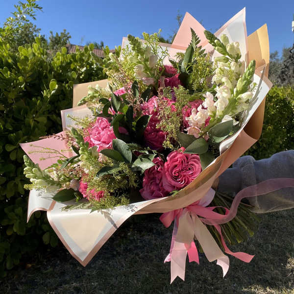 Bouquet of pink roses and white snapdragons wrapped in pastel paper