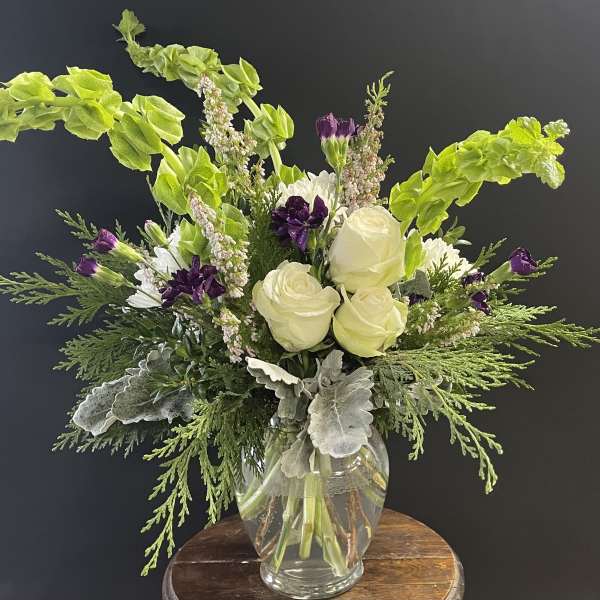 White roses and purple flowers in a clear glass vase with bright green foliage