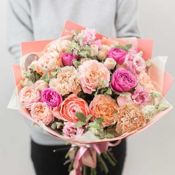 Handheld bouquet of pink and peach roses wrapped in coral paper