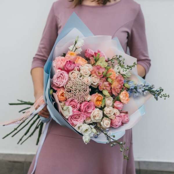Handheld bouquet of pink, peach, and white roses wrapped in pastel paper