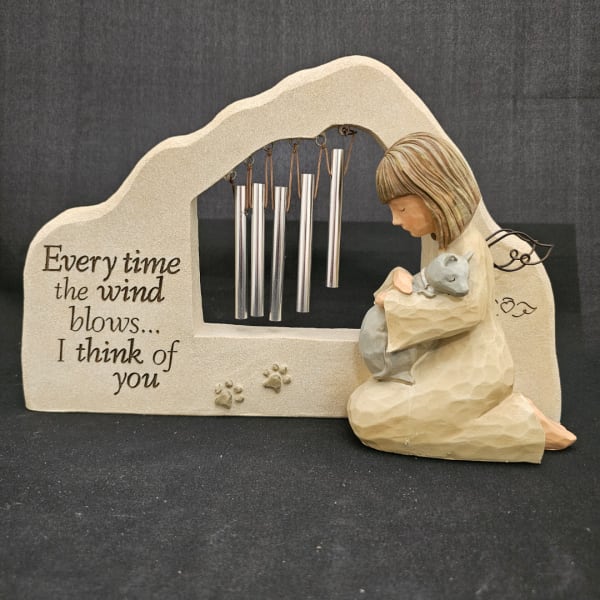 Angel figurine holding a cat beside a wind chime memorial plaque
