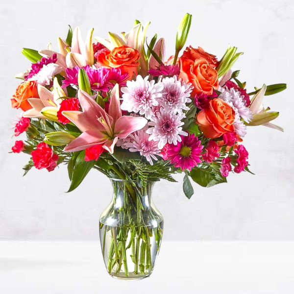 Mixed bouquet of pink and orange flowers in a clear glass vase