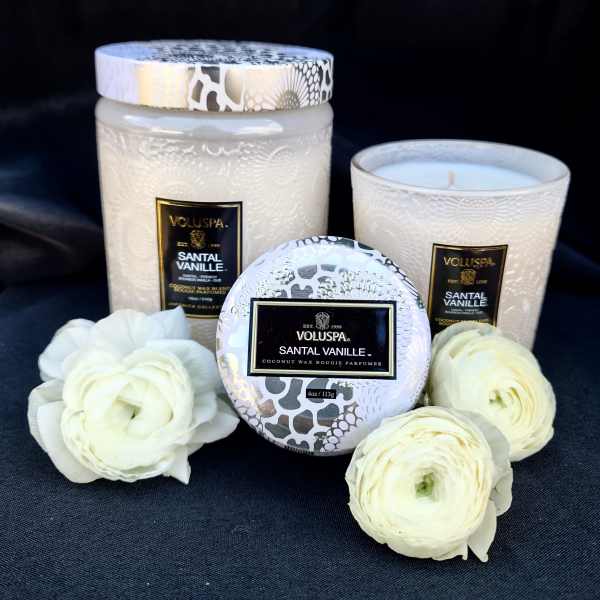 Three white candles with patterned lids and white ranunculus blooms.