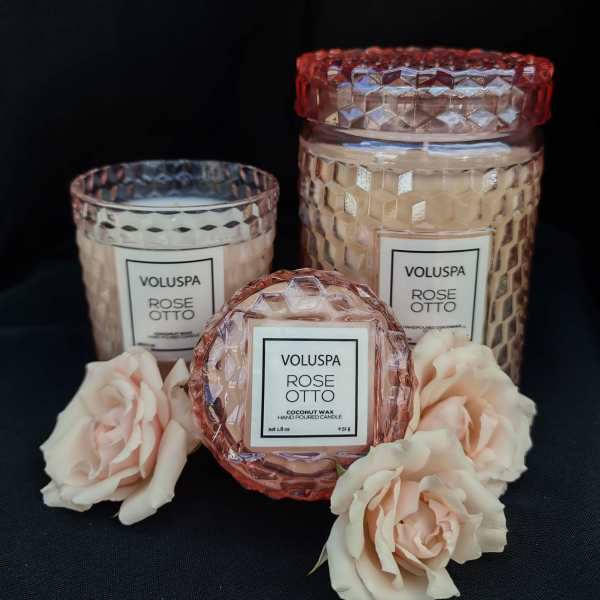 Three rose-scented candles with pale pink roses on a black background
