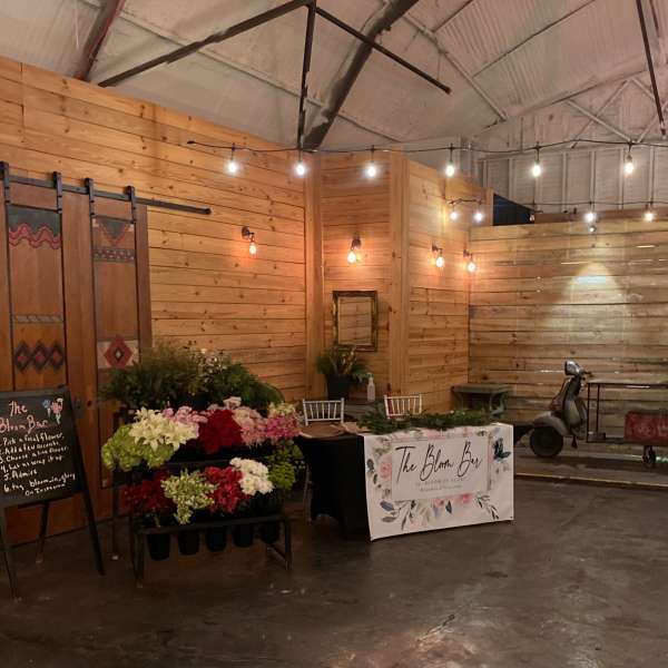 Rustic indoor flower bar setup with racks of mixed blooms and a scooter decorated with white and pink arrangements.