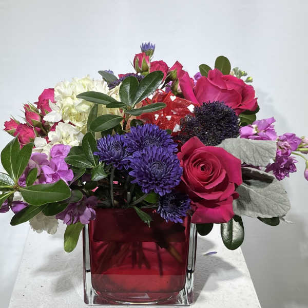 Pink and purple mixed flower arrangement in a red glass vase