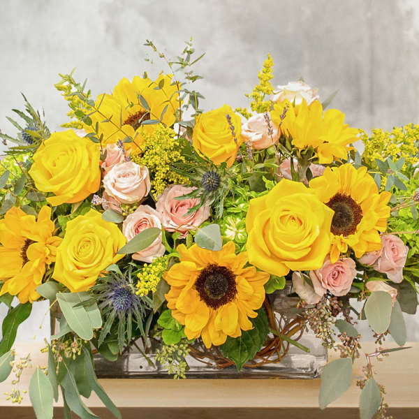 Yellow sunflowers and roses arranged in a glass vase