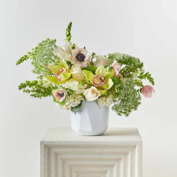 White vase with a pastel floral arrangement of orchids and roses