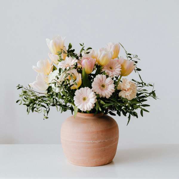 Pastel bouquet of tulips and daisies in a terracotta vase