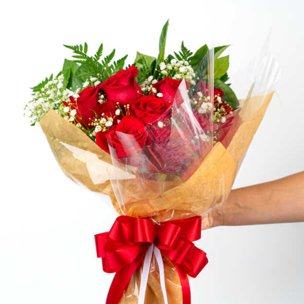 Handheld bouquet of red roses with white filler flowers wrapped in paper and cellophane with a red bow