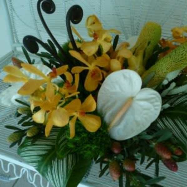 Low tropical arrangement with yellow orchids and white anthuriums among bold green foliage.