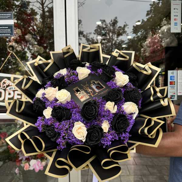 Bouquet of black and cream roses with purple filler and black-gold wrapping
