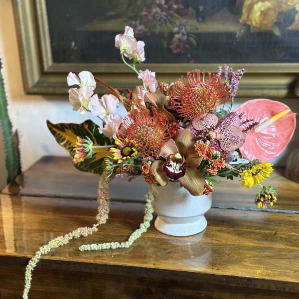 Tropical floral arrangement in a white vase with pink anthurium and orchids
