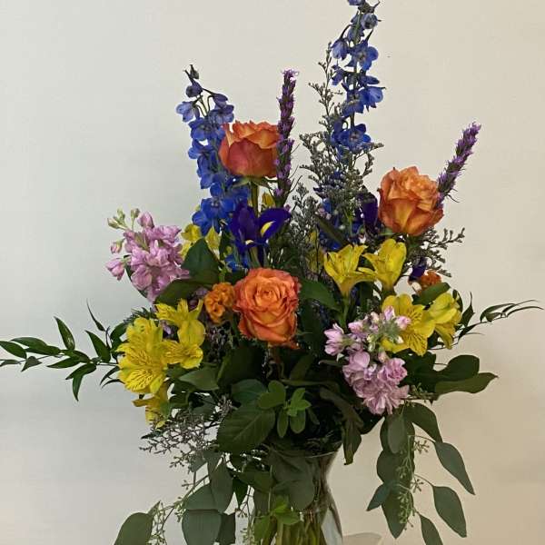 Mixed bouquet of orange roses, blue delphinium, and yellow alstroemeria in a glass vase