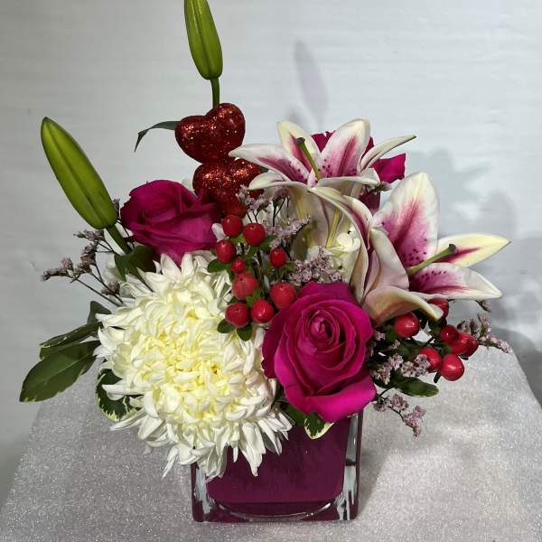 Pink roses and white lilies in a square glass vase with a white chrysanthemum