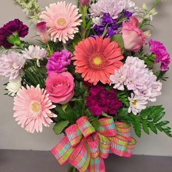 Mixed pink and purple flowers in a glass vase with a plaid ribbon