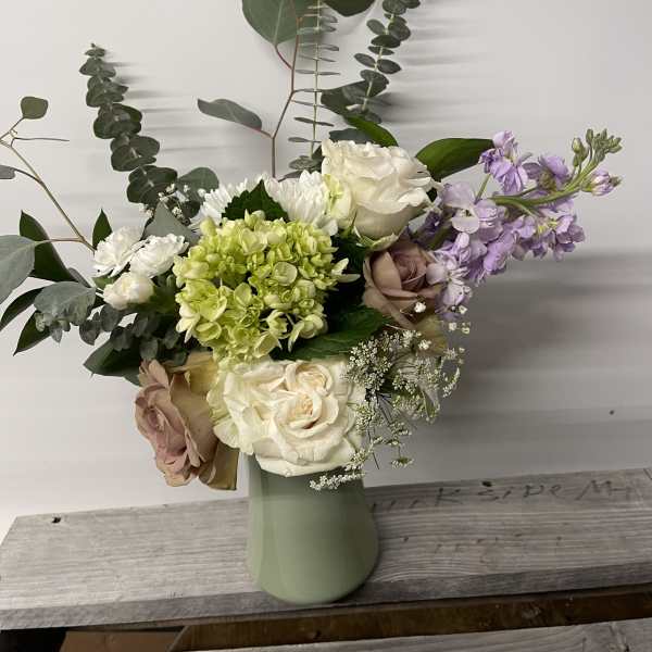 Mixed bouquet of roses, hydrangea, and lavender flowers in a pale green vase