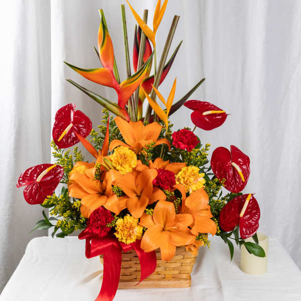 Tall tropical arrangement with orange lilies, yellow and red carnations, and red anthuriums in a woven basket