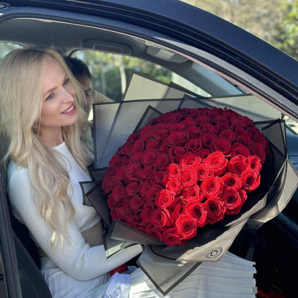 Woman holding a large bouquet of red roses in a car