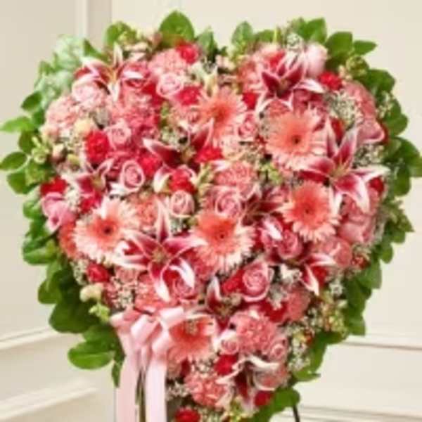Heart-shaped pink and red floral standing arrangement with roses, lilies, and gerbera daisies on a stand
