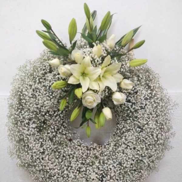 Large white wreath of baby's breath with white lilies and roses on a stand