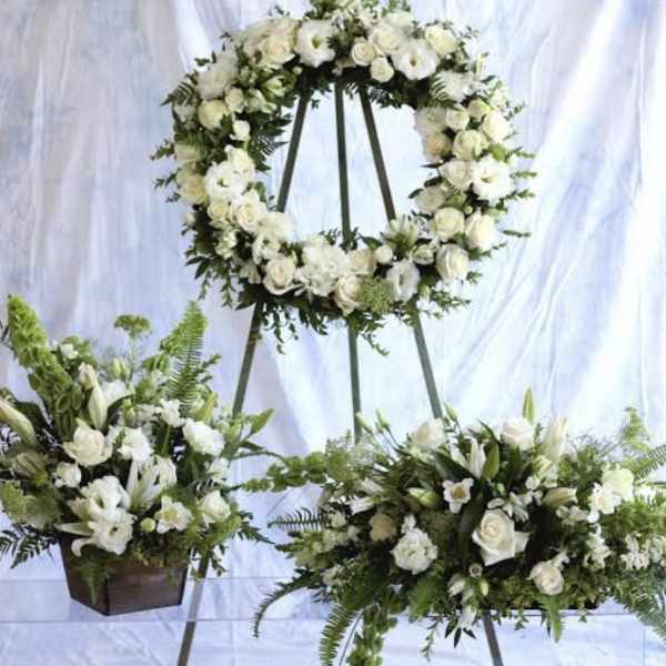 White wreath, spray, and matching floral arrangement on stands with green accents for a sympathy display.