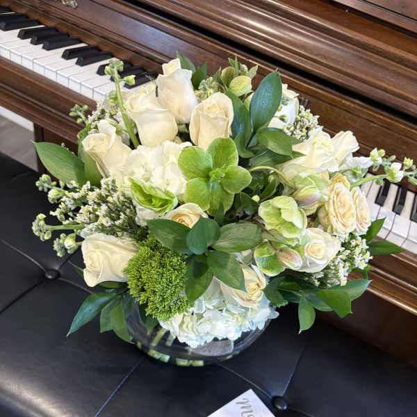 White rose and green floral arrangement in a glass vase on a piano bench
