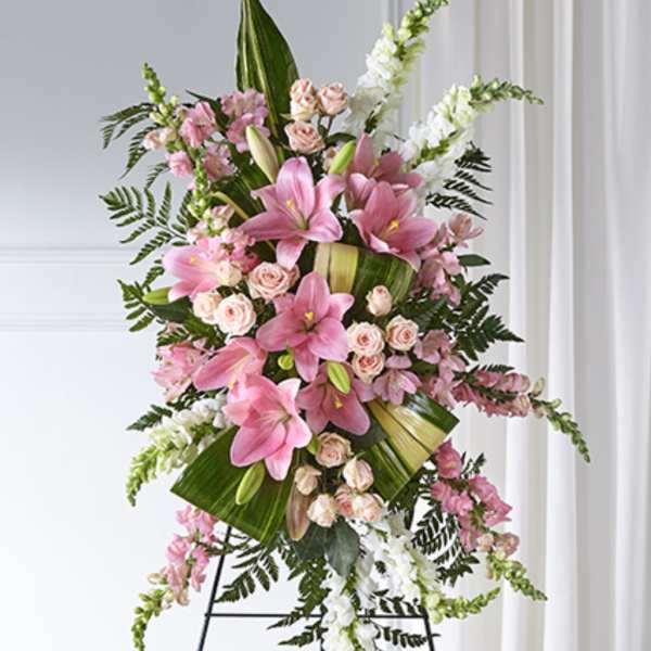 Tall standing spray with pink lilies, pale spray roses, and white snapdragons on a metal easel