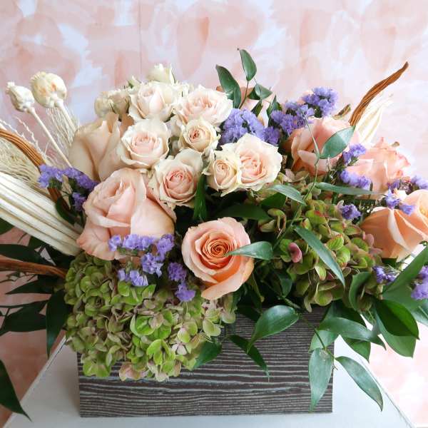 Peach roses and purple filler flowers in a rectangular vase