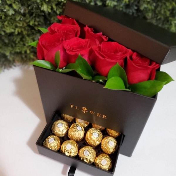 Red roses in a black gift box above gold-wrapped chocolates
