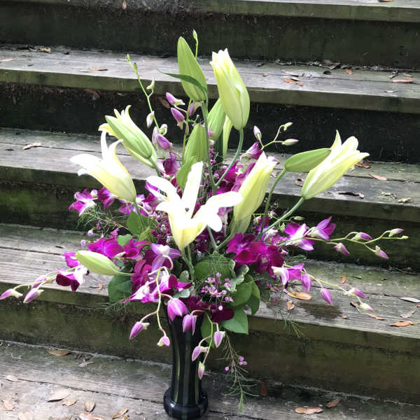 Tall floral arrangement with white lilies and purple orchids in a black vase