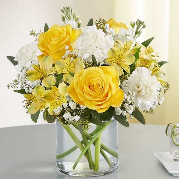 Yellow roses and white flowers arranged in a clear glass vase