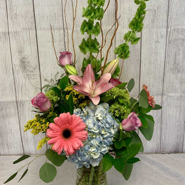 Tall mixed bouquet in a glass vase with pink lilies, roses, hydrangea, and gerbera daisies