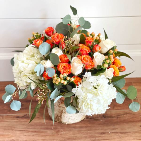 Bouquet of orange and white roses with white hydrangeas in a rustic container