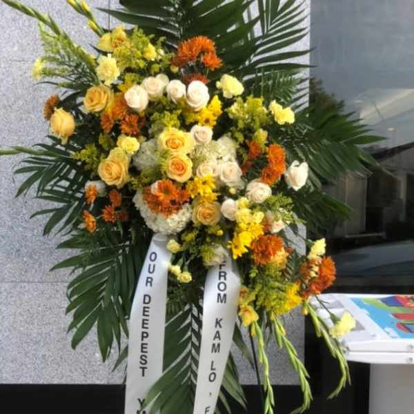Large standing floral wreath with yellow, white, and orange flowers