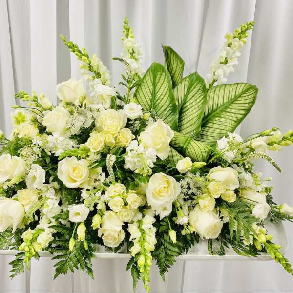 White floral casket spray with roses and snapdragons
