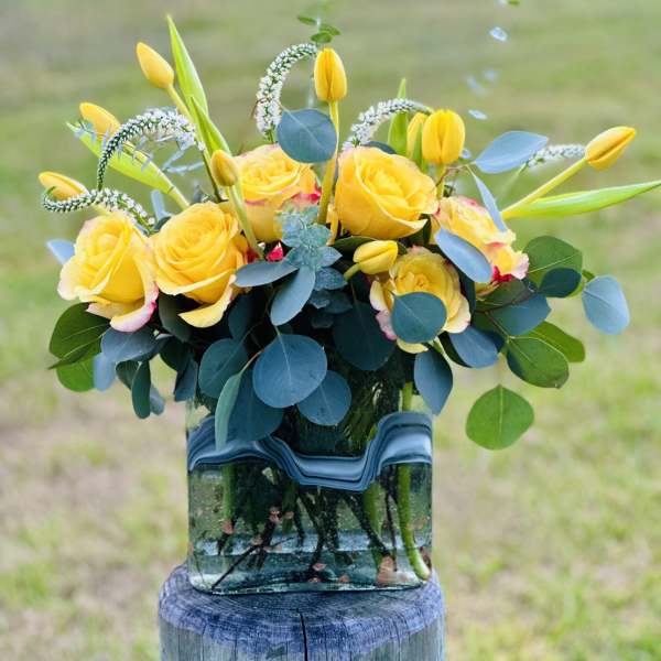 Yellow roses and tulips arranged in a glass vase