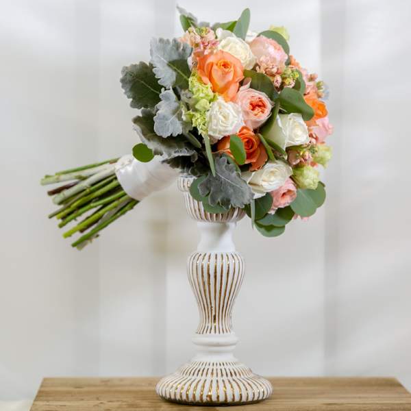 Bouquet of peach, white, and pink roses in a white pedestal vase
