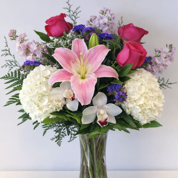 Bouquet of pink roses, lilies, hydrangeas, and orchids in a glass vase