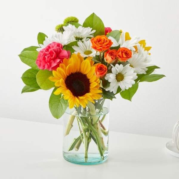 Mixed bouquet with a sunflower, daisies, roses, and carnations in a glass vase