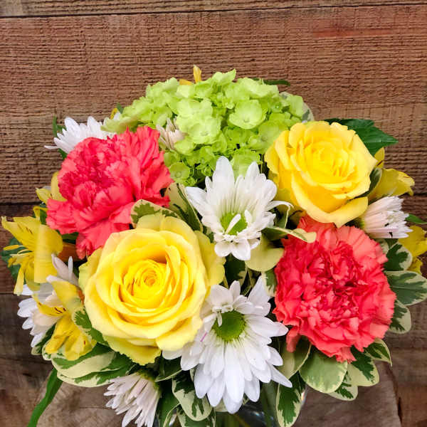 Bouquet of yellow roses, red carnations, white daisies, and green hydrangea in a glass vase
